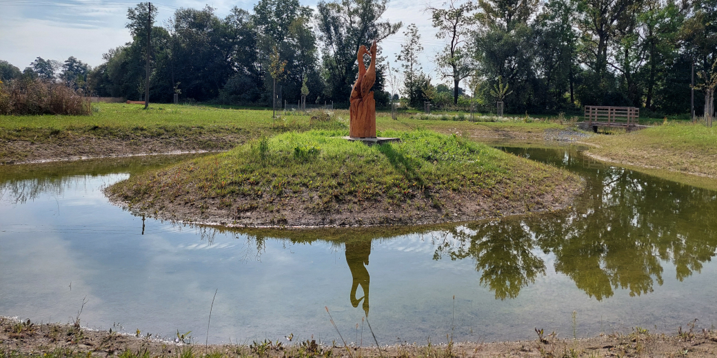 Nově vybudovaný mokřad v Malém Újezdu má uprostřed ostrůvek, na kterém je umístěna dřevěná socha čápa.